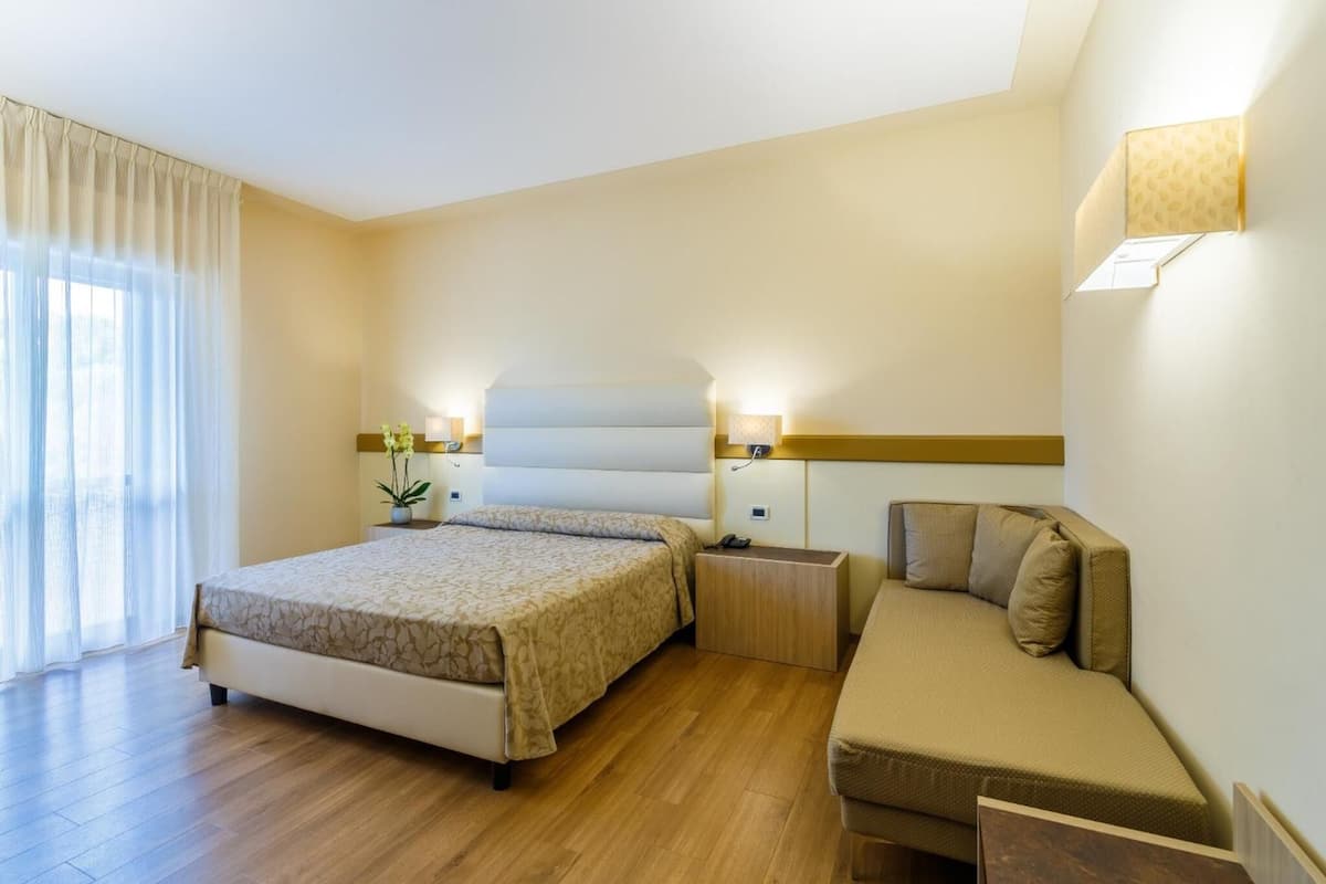 A hotel room with a bed, a sofa, a nightstand, and a lamp.