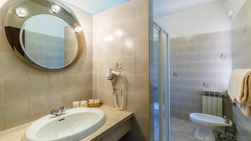Un bany amb un mirall rodó, un lavabo, un vàter i una zona de dutxa.