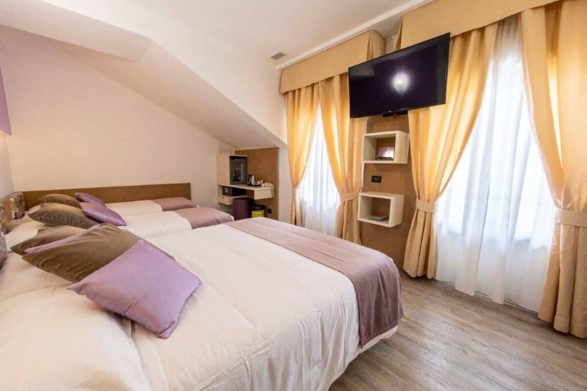Habitación de hotel con dos camas, televisor y estante con artículos de aseo.