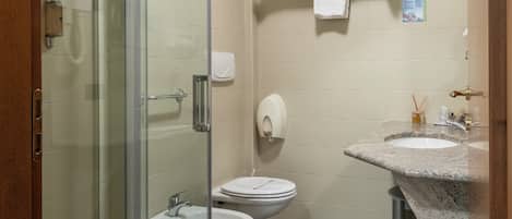 Un baño moderno con cabina de ducha de vidrio, inodoro blanco y lavamanos de granito.
