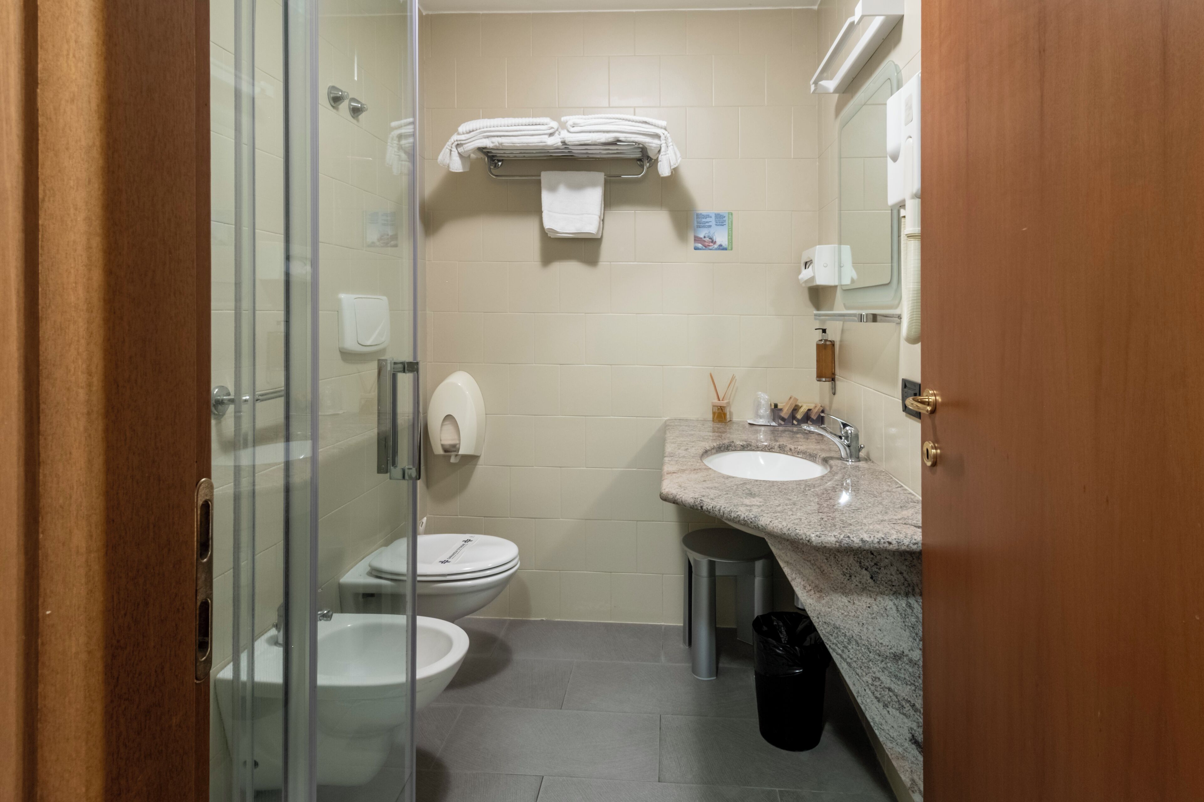 Kompakti kylpyhuone, jossa on lasinen suihkuseinä, wc, marmoritasoinen pesuallas ja pyyheteline, jossa on siististi taitellut pyyhkeet.