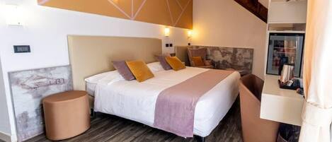 A modern hotel room with a large bed, a wooden floor, a built-in bench, and a ceiling light fixture.