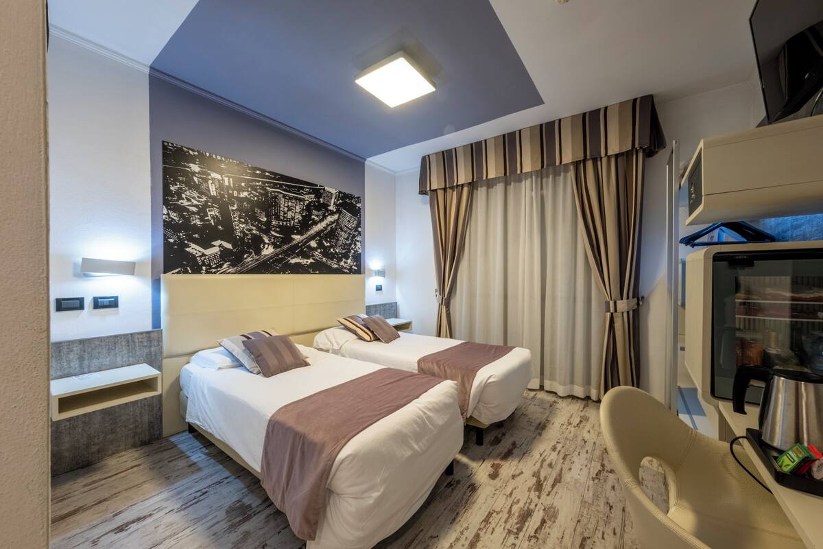 Habitación de hotel con dos camas, un cuadro grande con un paisaje urbano en la pared, un televisor de pantalla plana y un minibar.