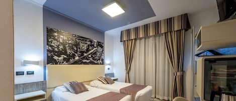 A hotel room with two beds, a large cityscape artwork on the wall, a flat-screen TV, and a minibar.