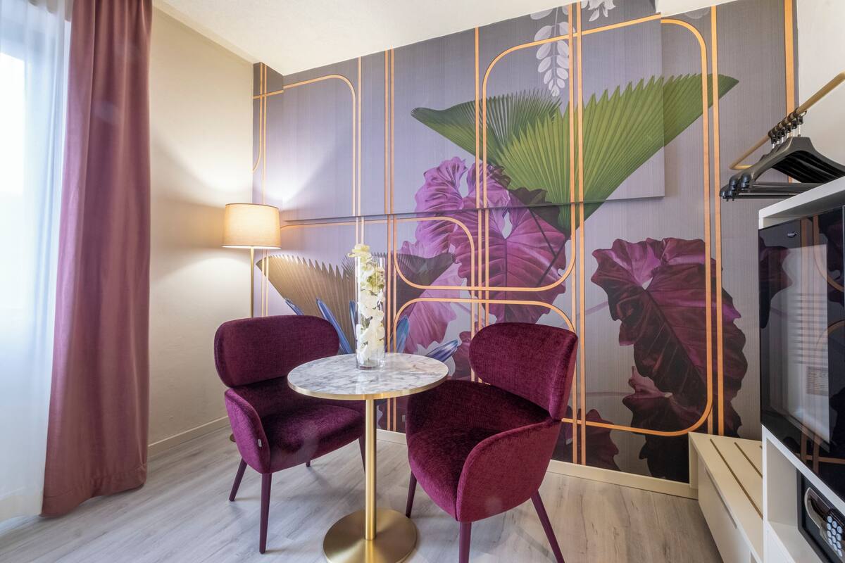 Una habitación con una mesa redonda y dos sillas, una lámpara y un papel tapiz con motivos florales.
