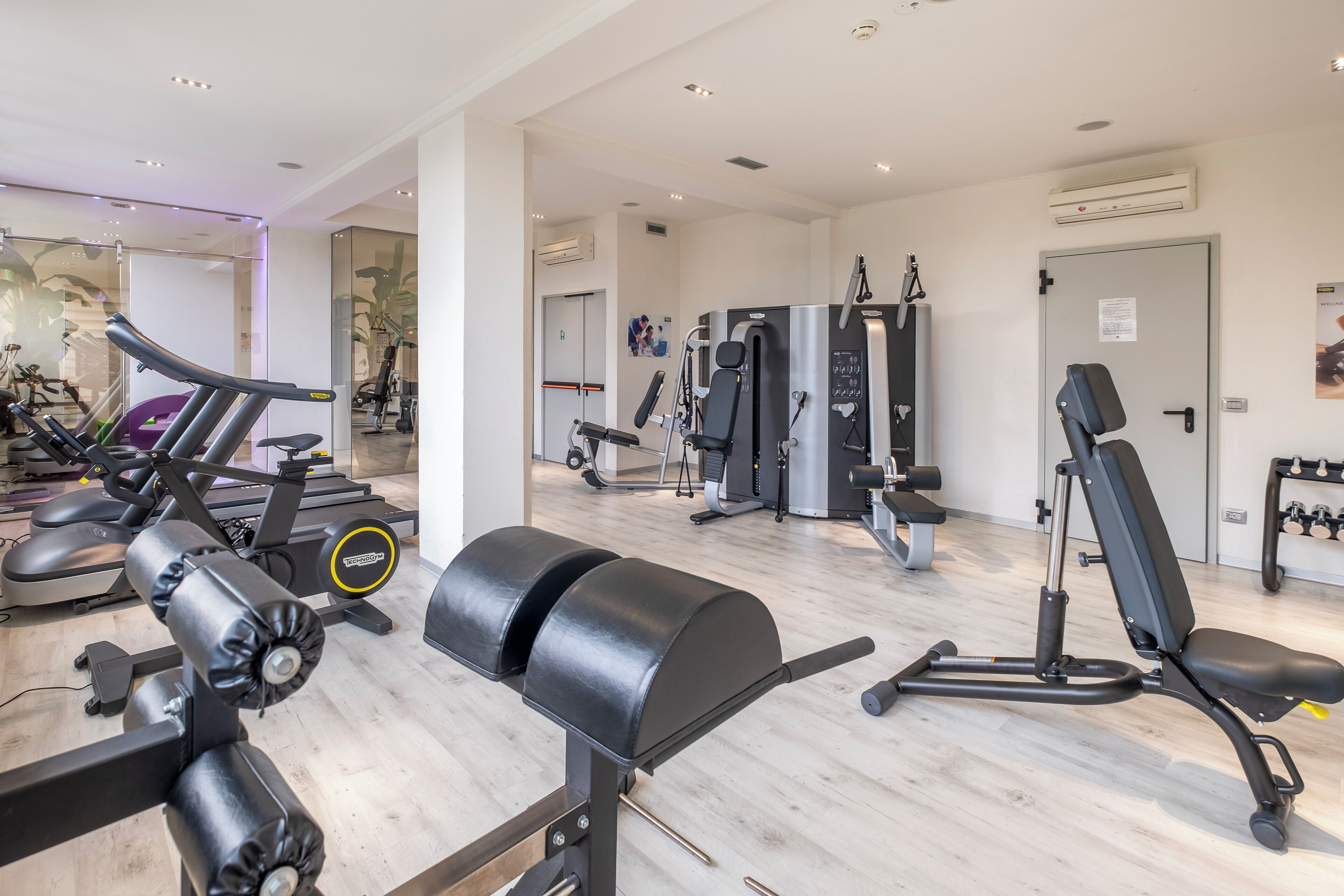 A gym with various exercise equipment, including treadmills, weight machines, and a bench.