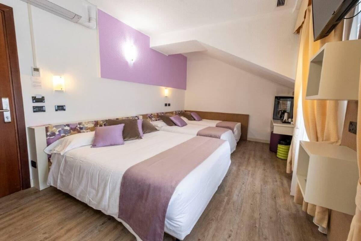 Habitación de hotel con dos camas, piso de madera, pared de acento morada y un pequeño escritorio con espejo.