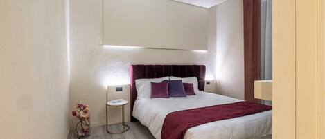 Una habitación de hotel moderna con una cama grande, una mesita de noche y una pequeña mesa auxiliar.
