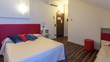 Ein Hotelzimmer mit einem großen Bett, einem kleineren Bett, einer roten Akzentwand, einem roten Hocker und einer wandmontierten Klimaanlage.