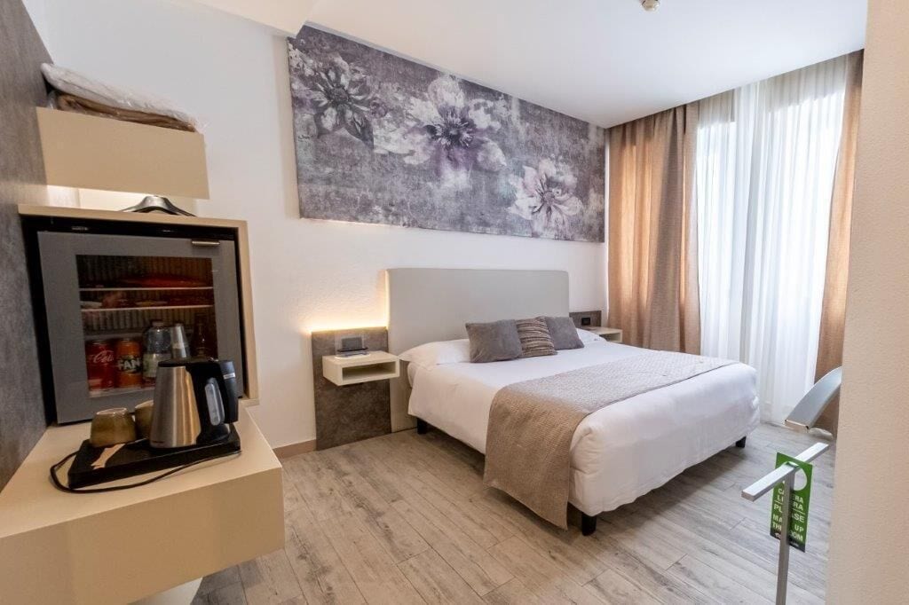 A hotel room with a bed, bedside table, lamp, and a wall-mounted artwork.
