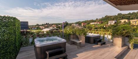 A rooftop terrace with a hot tub, seating area, and a view of a hillside town.