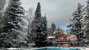 A swimming pool surrounded by snow-covered trees and a brick building. - Hotel San Francisco (Chacras de Coria)
