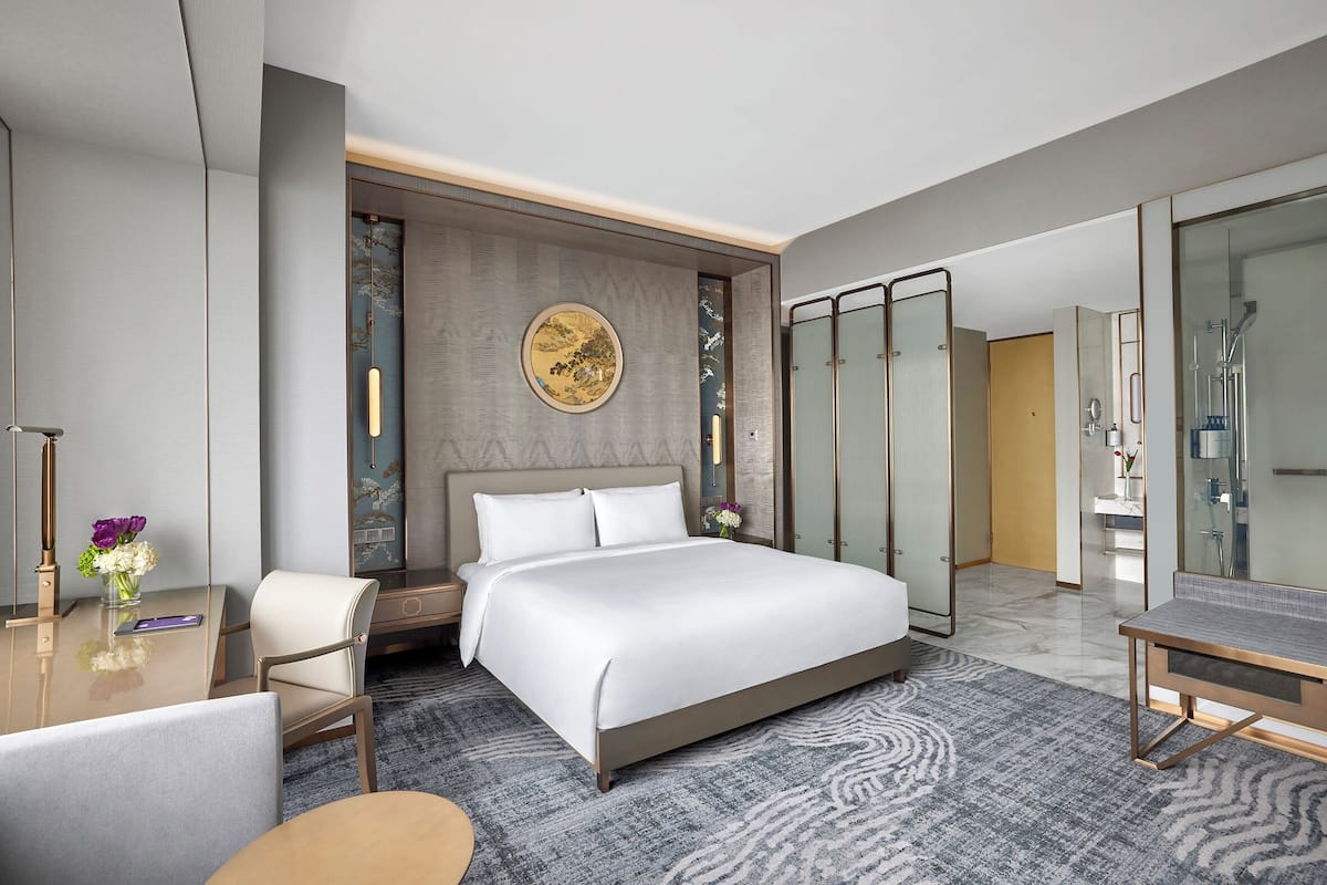 Una habitación de hotel moderna con una cama grande, un escritorio con una silla, una tocador con espejo y una zona de ducha.