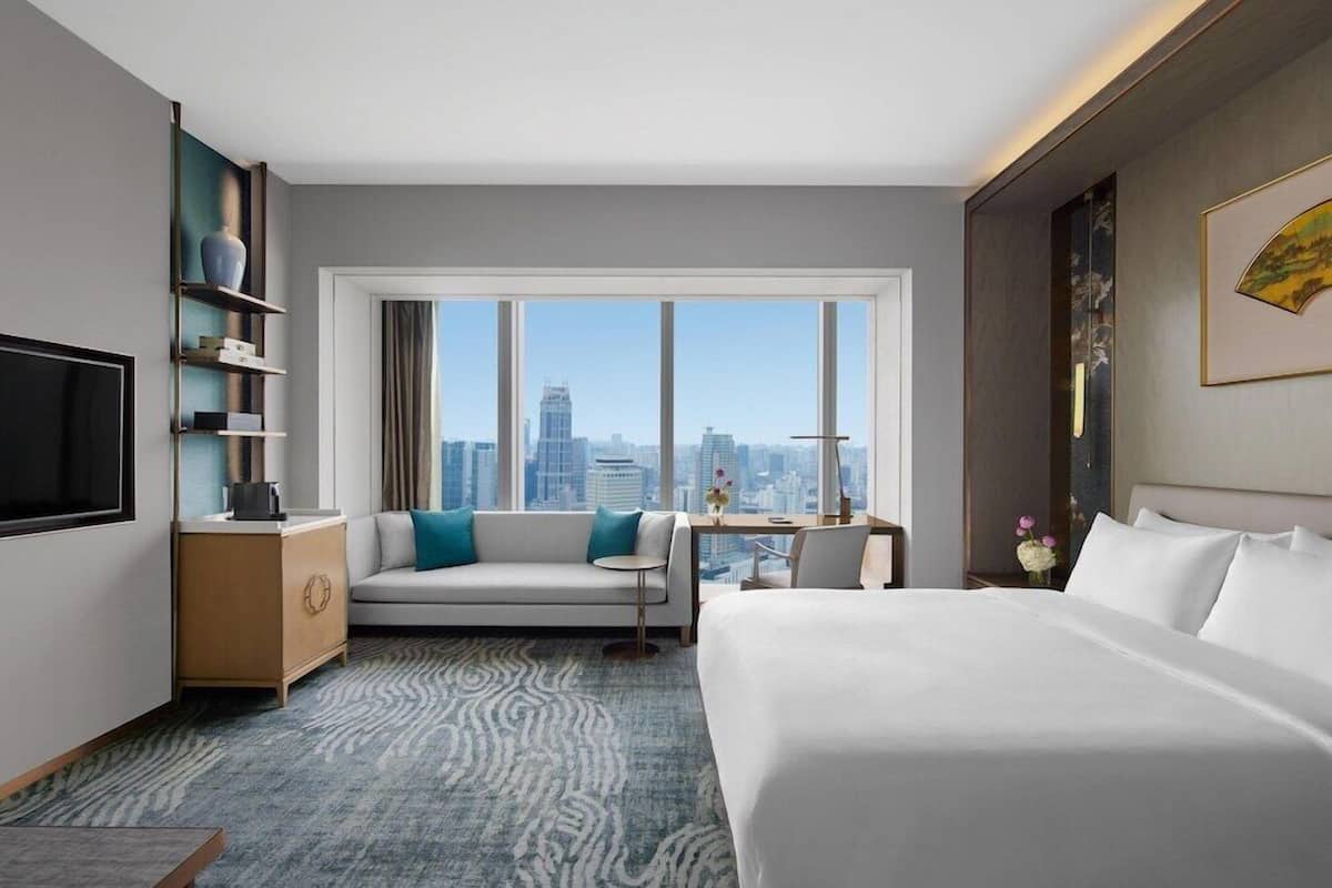 Una habitación de hotel con cama, sofá, escritorio, televisor y vista a la ciudad.