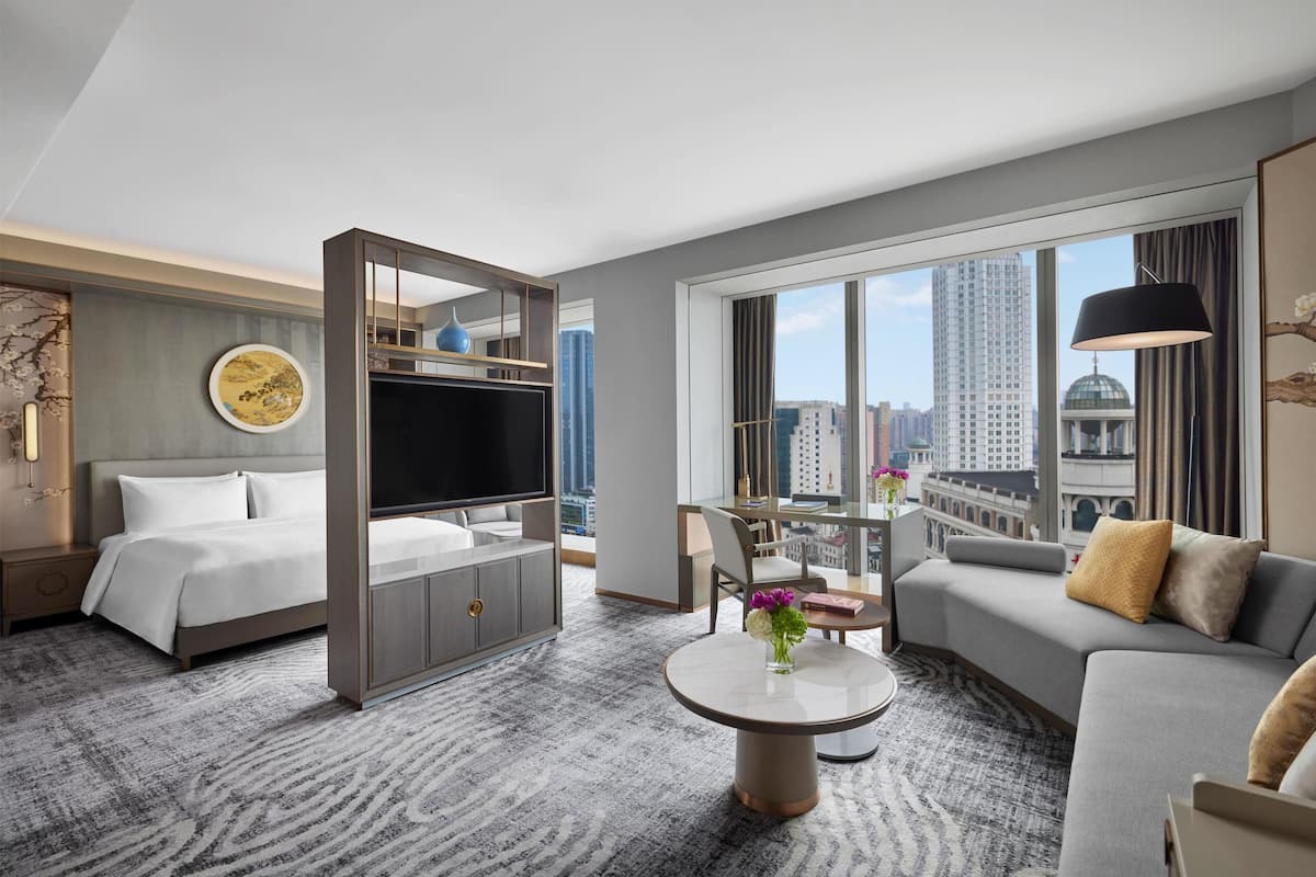 Habitación de hotel con cama, televisión, sofá, mesa de comedor y vista a la ciudad.