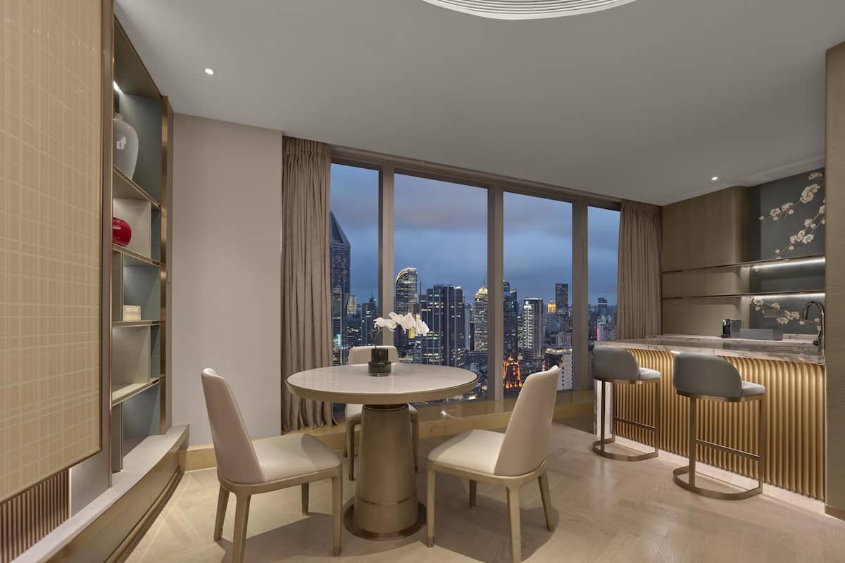 Una habitación de hotel moderna con zona de comedor, cocina y un amplio ventanal con vistas a la ciudad.