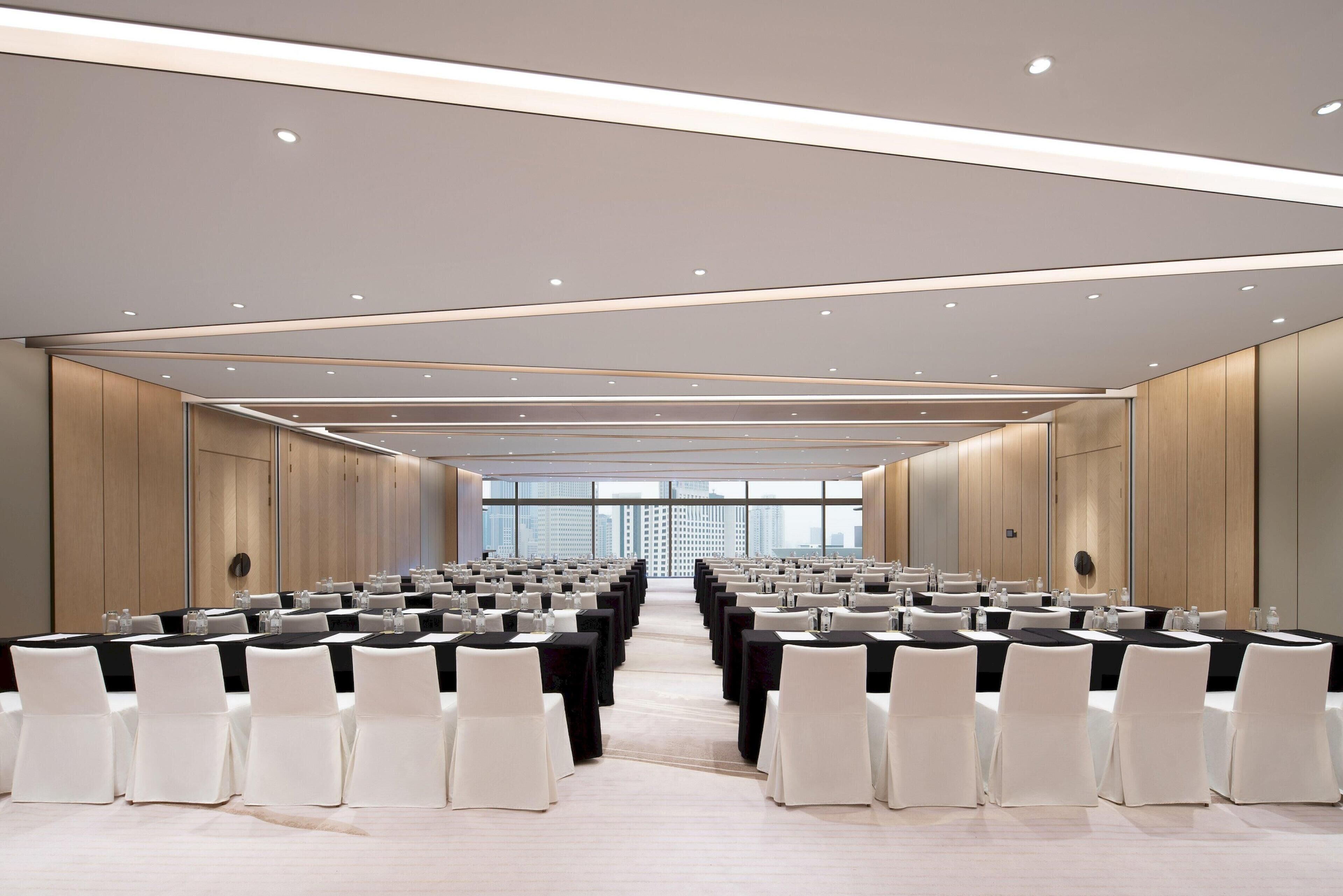 A conference room with rows of tables and chairs, large windows, and a modern ceiling design.