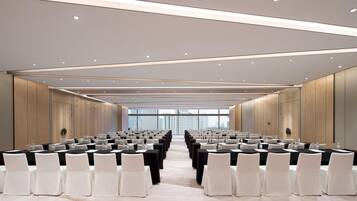A conference room with rows of tables and chairs, large windows, and a modern ceiling design.