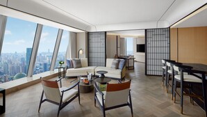 Habitación de hotel moderna con vistas a la ciudad, un sofá, sillas, una mesa de comedor y una zona de cocina.