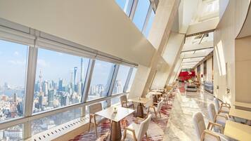 A modern hotel interior with a dining area, large windows, and a city view.