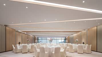 A spacious banquet hall with round tables, white chairs, and floral centerpieces.