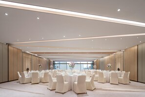 A spacious banquet hall with round tables, white chairs, and floral centerpieces. - Conrad Shanghai (Shanghai)