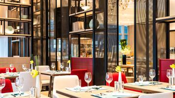 A modern restaurant interior with tables set for dining, red upholstered chairs, and decorative elements like flowers and vases.