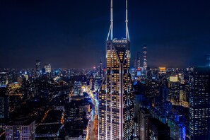 A nighttime cityscape with illuminated skyscrapers, including a prominent building with two vertical structures and the name 'Shima' visible.