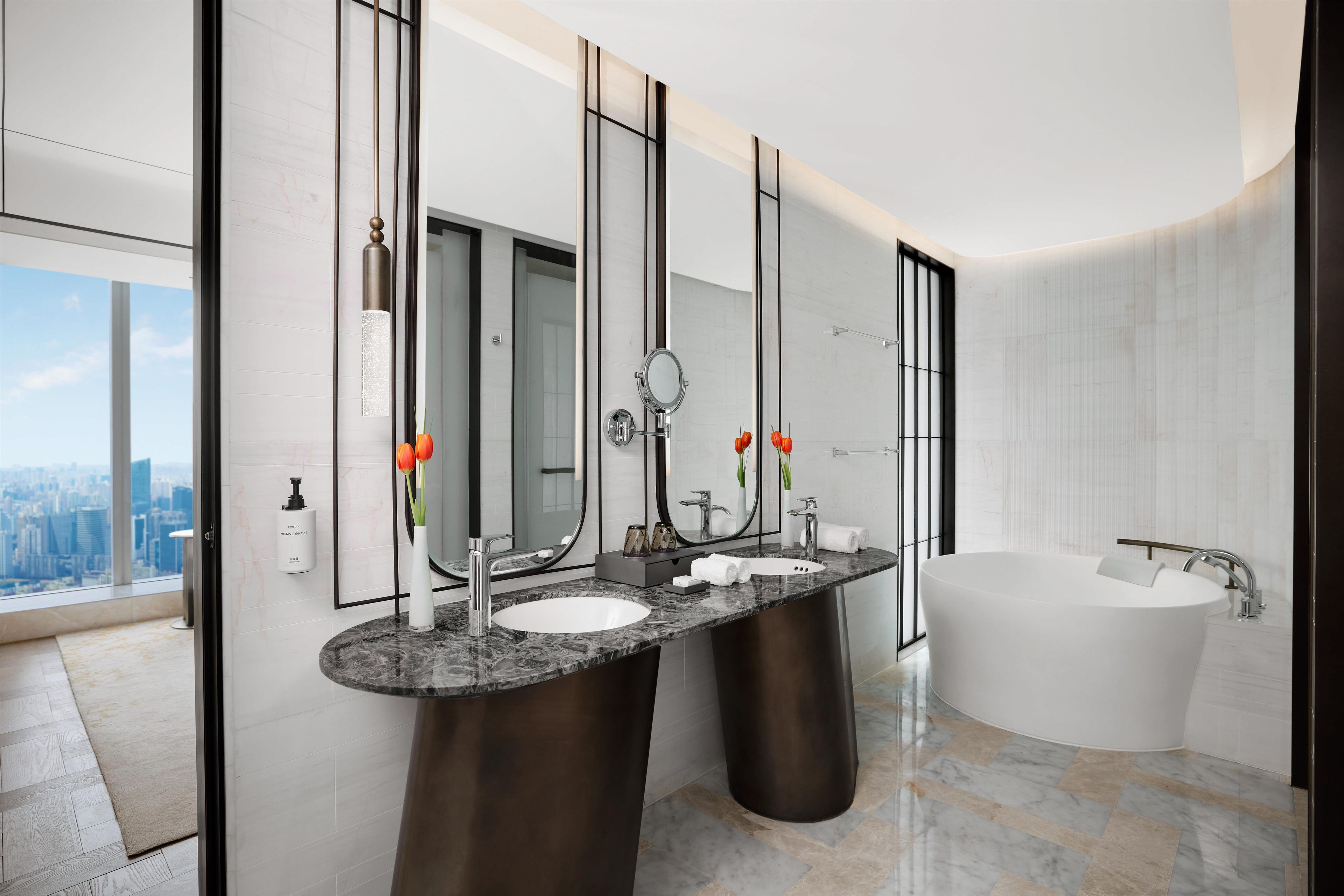 A modern bathroom with dual sinks, a large mirror, and a freestanding bathtub.