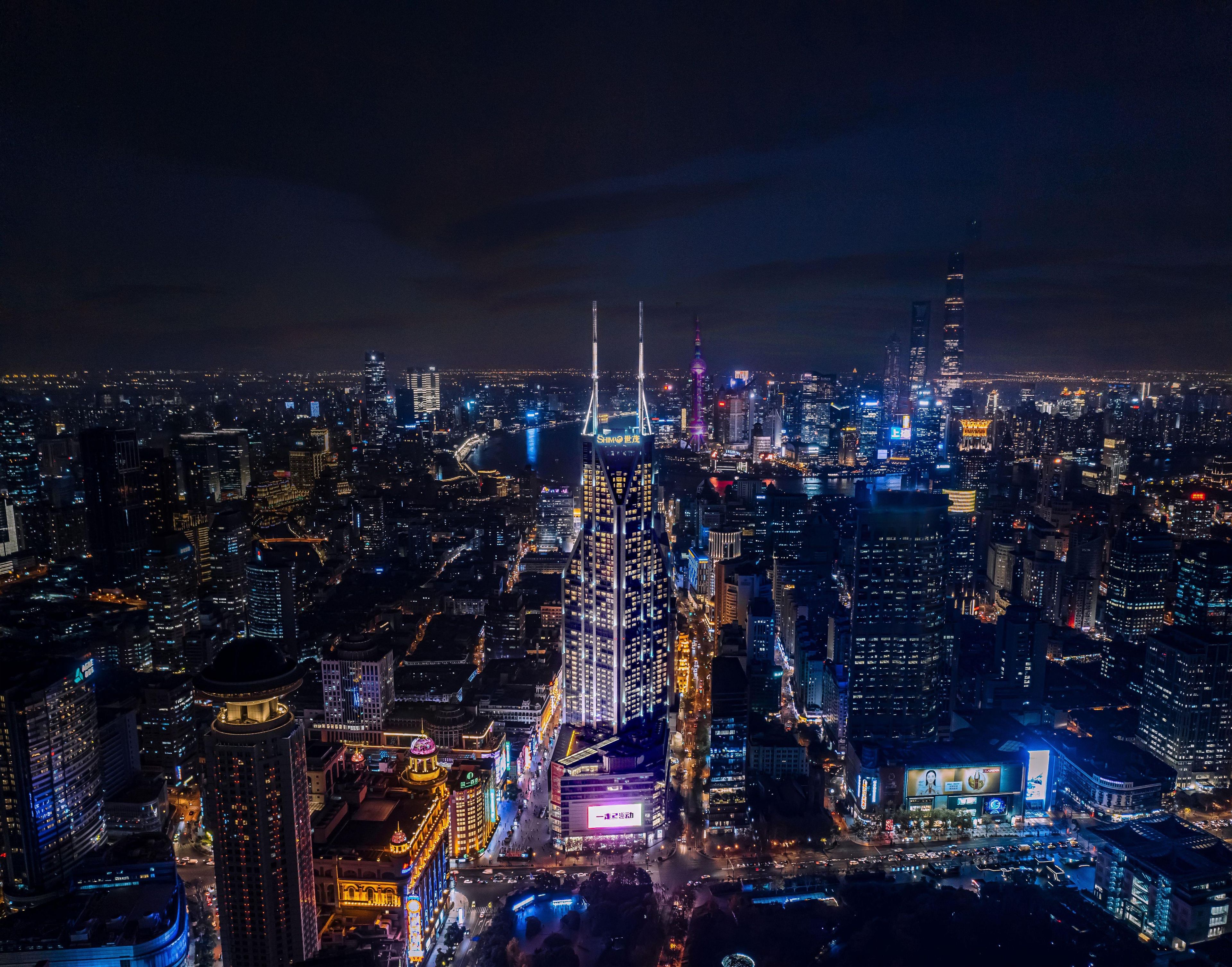 A nighttime cityscape with illuminated skyscrapers and a river.