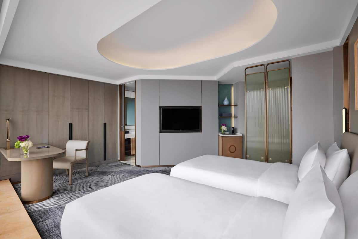 Una habitación de hotel moderna con una cama grande, un escritorio con una silla, un televisor y un armario.
