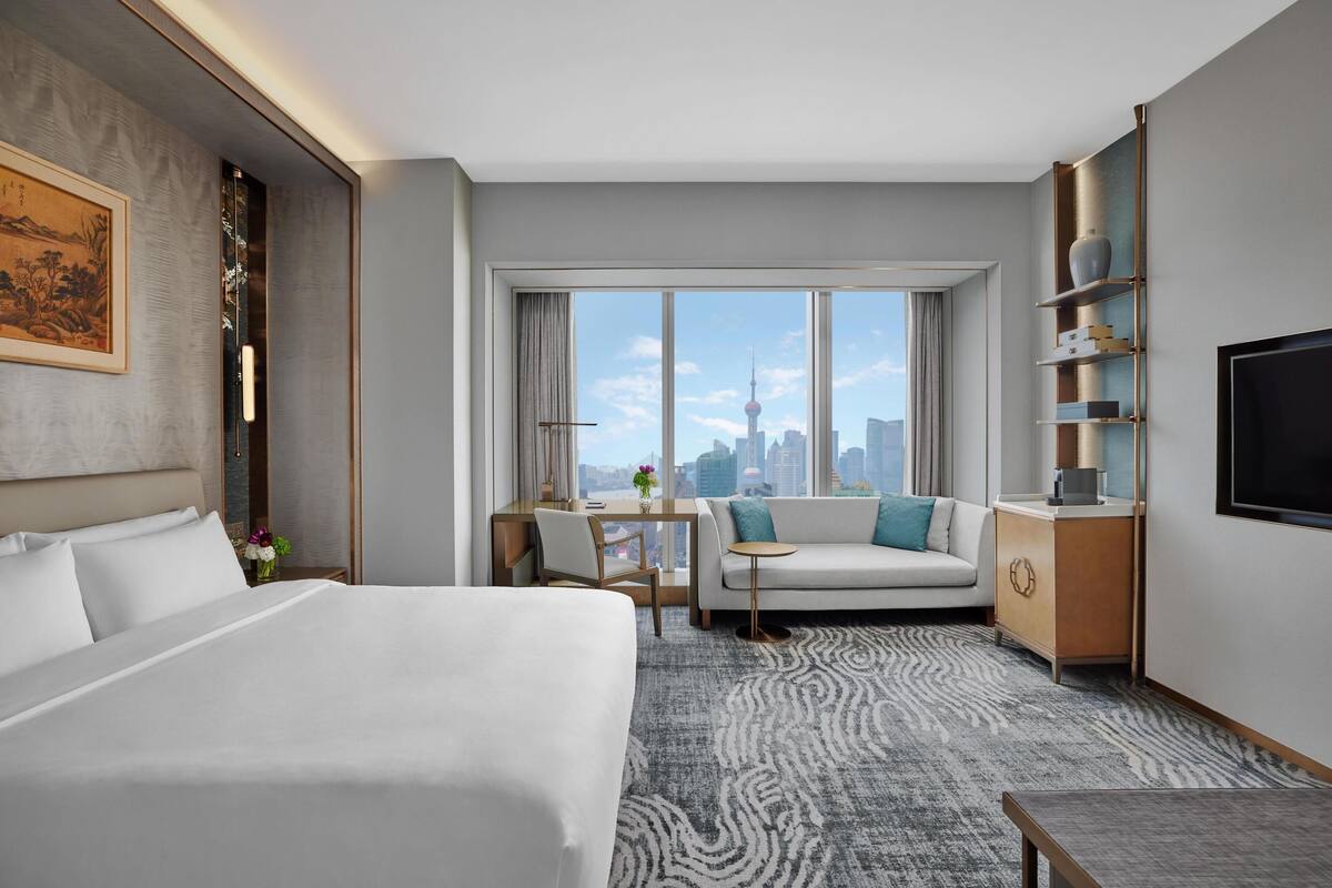 Habitación de hotel con cama, sofá, televisión y vista a la ciudad.