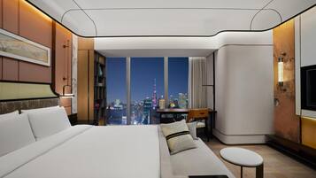 Una camera d'albergo moderna con un ampio letto, una zona salotto, una scrivania e vista sulla città.