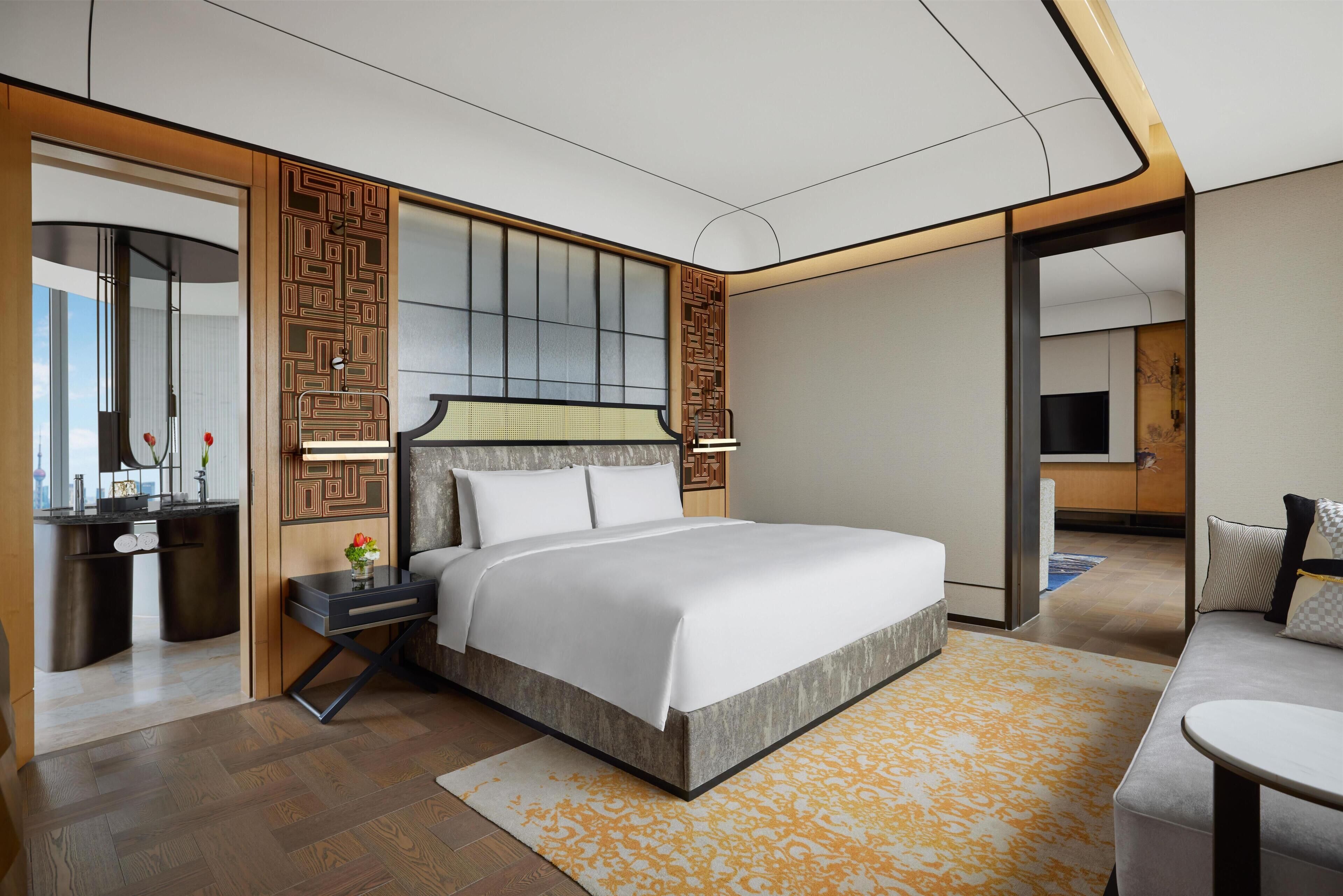 A modern hotel room with a large bed, a desk with a mirror, a TV, and a sofa.