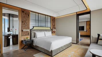 A modern hotel room with a large bed, a desk with a mirror, a TV, and a sofa.