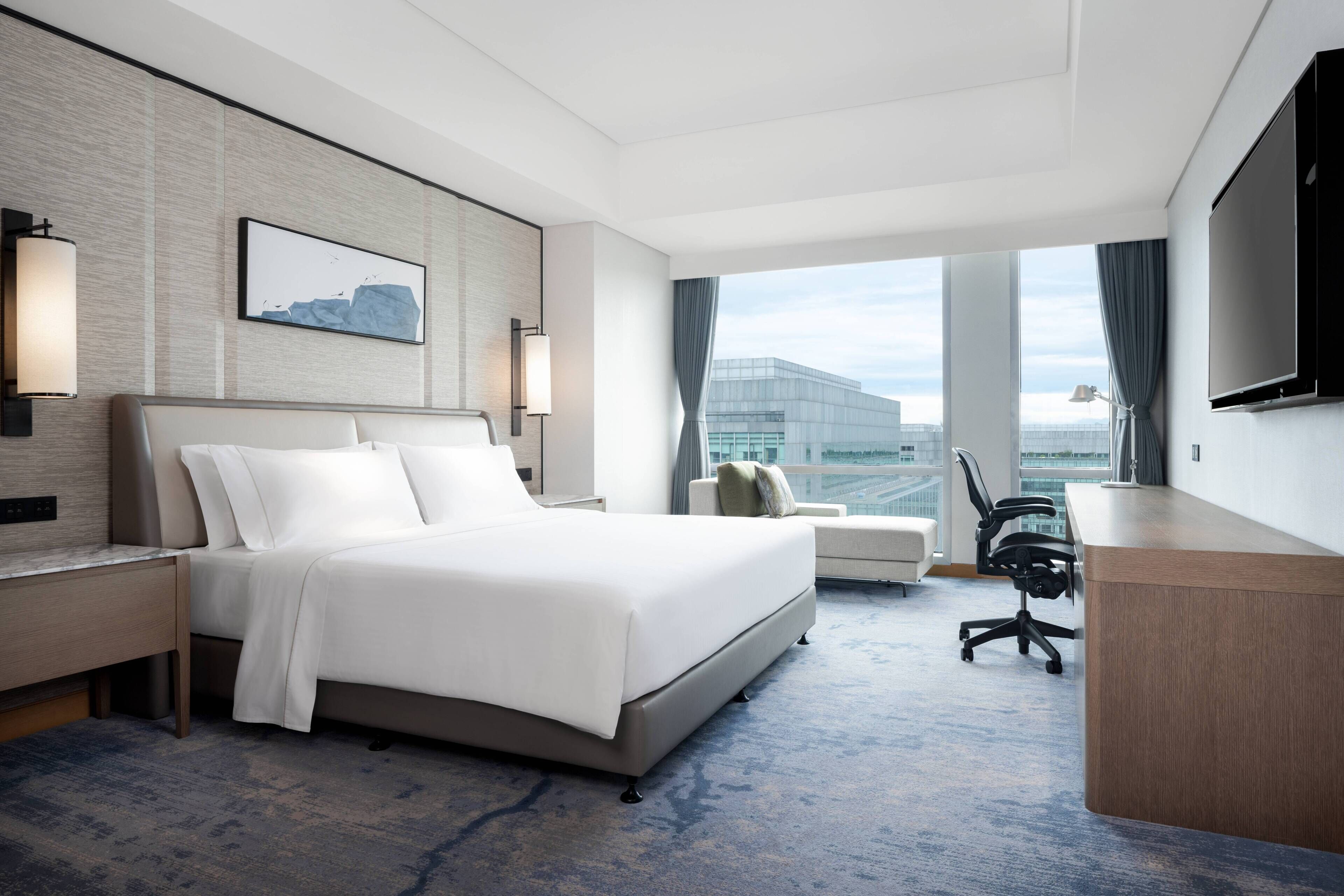 A modern hotel room with a large bed, a desk, a chair, and a television.