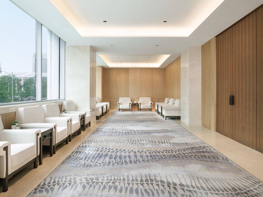 A modern hotel lobby with a long reception desk, white leather chairs, and a patterned carpet.