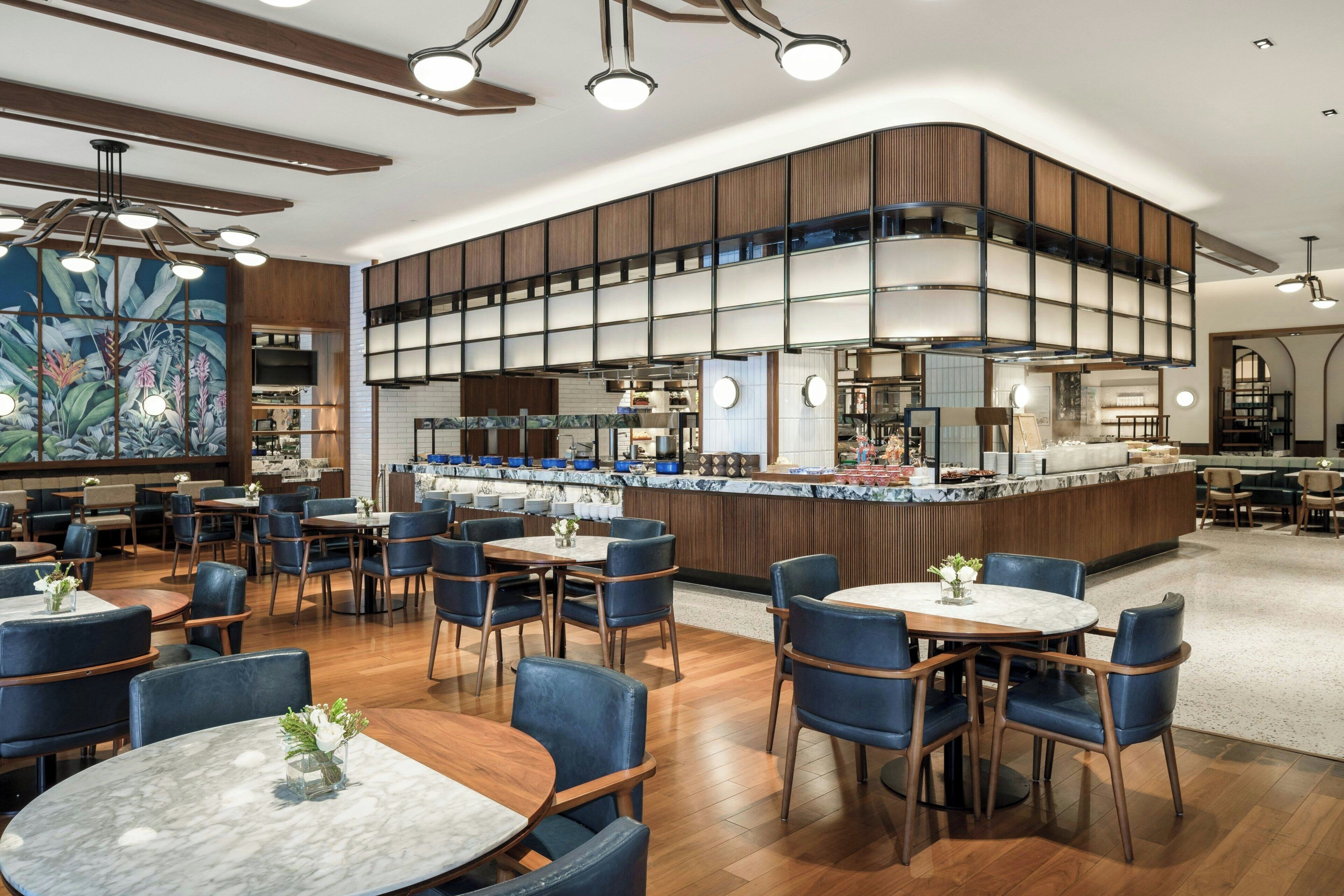 Ein modernes Restaurant mit einer zentralen Bar, mehreren Sitzbereichen und einer dekorativen Wandmalerei.