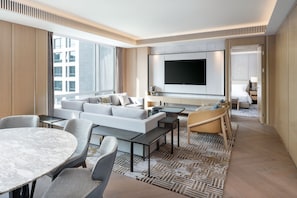 Une chambre d’hôtel moderne dotée d’un grand téléviseur à écran plat, d’un canapé, d’une table à manger et d’un tapis à motifs.