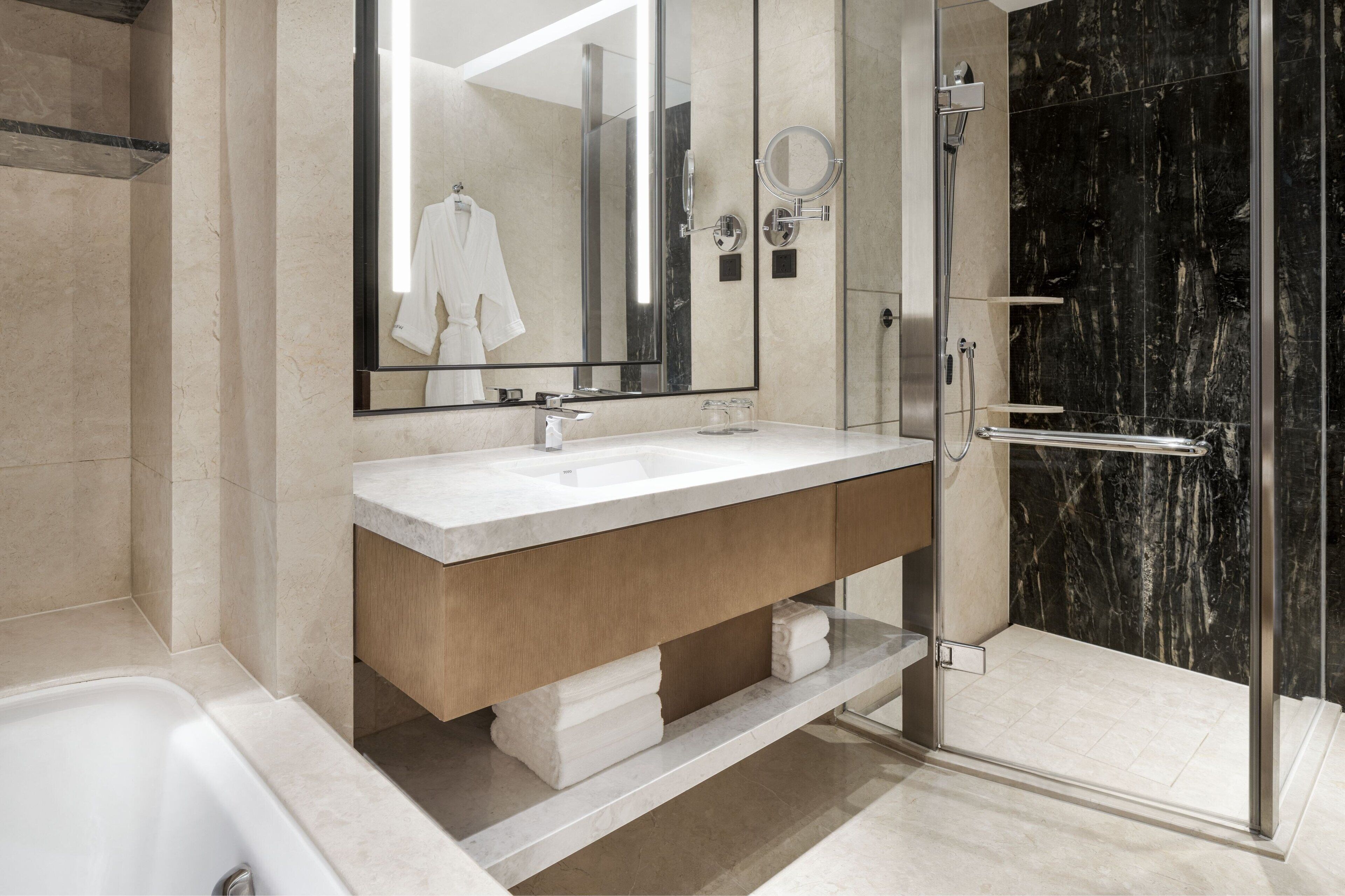 A modern bathroom with a large mirror, two sinks, a shower, and a bathtub.