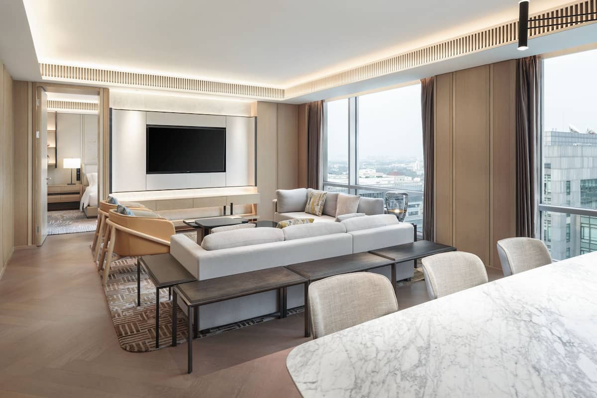 A modern hotel room with a large sofa, a dining table, and a TV mounted on the wall.