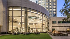Un bâtiment moderne doté d’une façade en verre incurvée, d’un atrium central et d’un espace extérieur aménagé avec des jardinières.