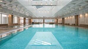 Une grande piscine intérieure dotée d’un haut plafond et de lucarnes, entourée de murs au design moderne.