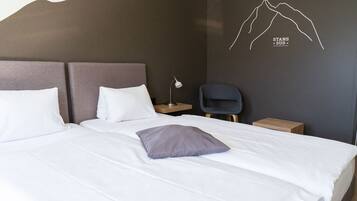 Una cama bien tendida con ropa de cama blanca y gris, una sola almohada gris y un diseño de montaña en la pared.