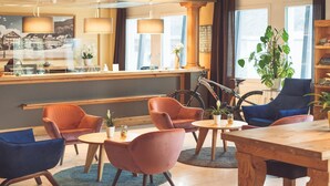 Eine Hotelhalle mit Rezeption, Sitzbereich mit Sesseln, einem Fahrrad und einer großen Pflanze.