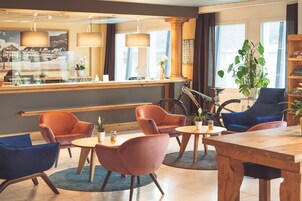 Un vestíbulo de hotel con mostrador de recepción, zona de estar con sillas, una bicicleta y una planta grande.