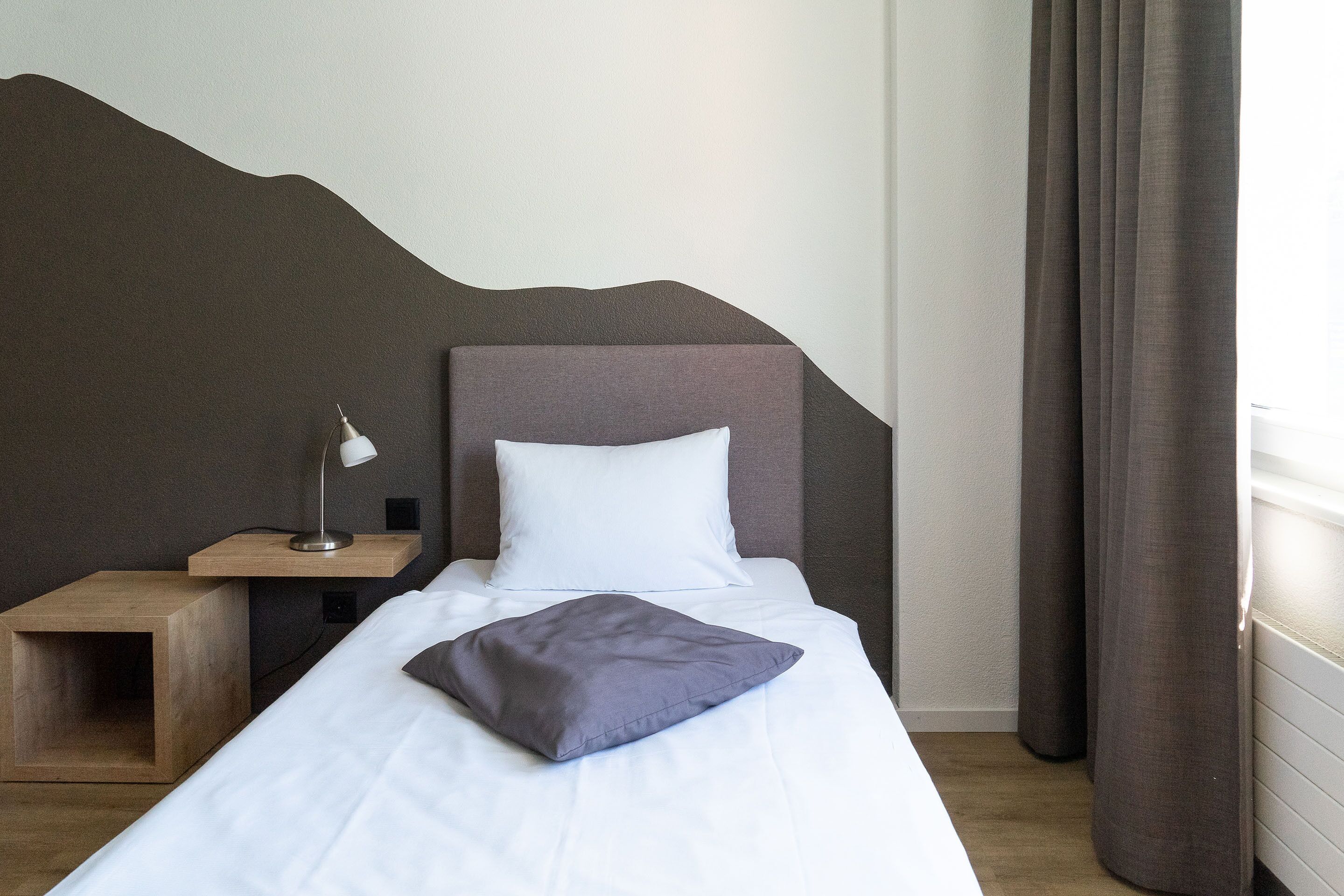 A neatly made bed with a pillow, a bedside lamp, and a wooden nightstand.