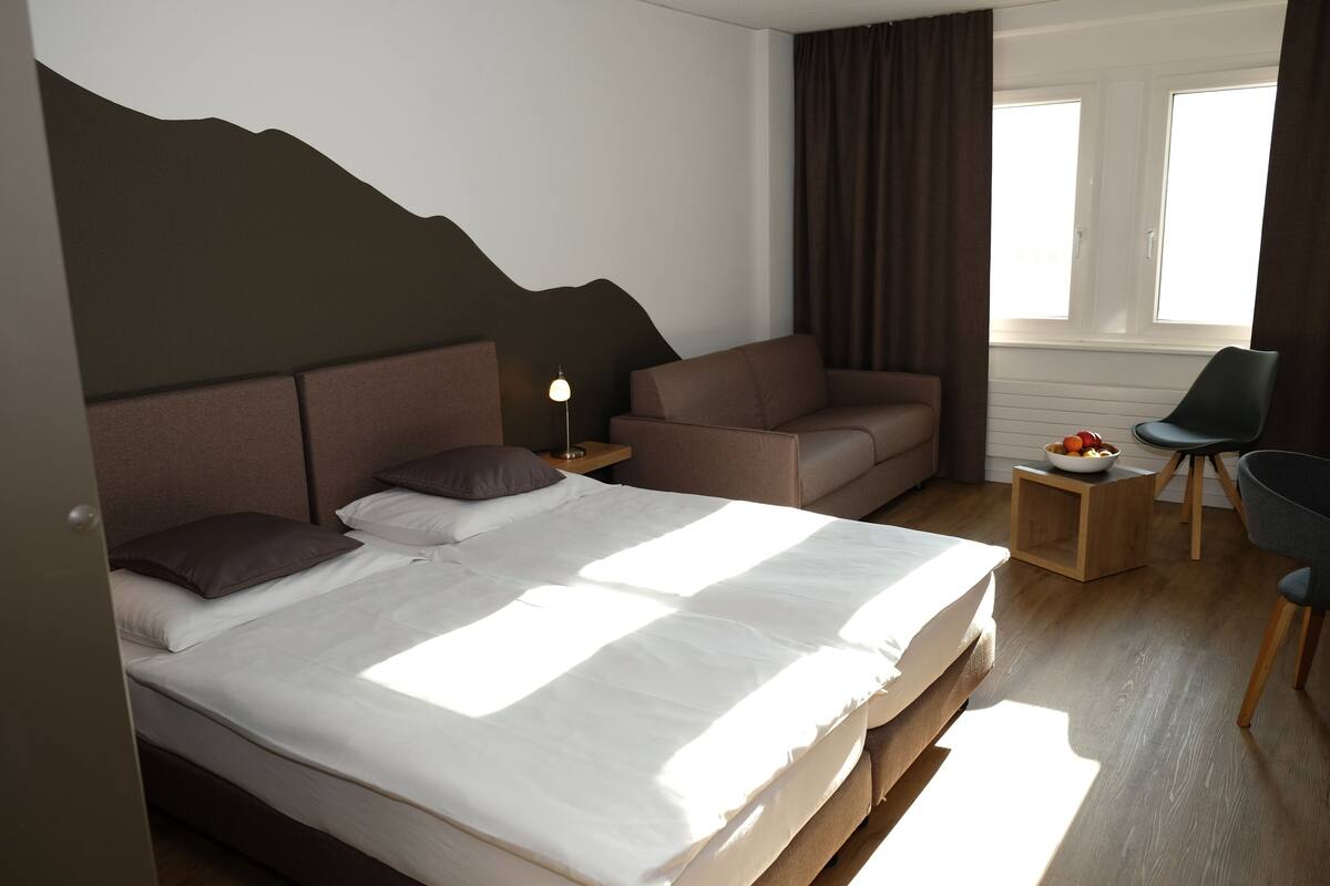 Una habitación de hotel moderna con una cama, un sofá, una silla y una mesita con fruta.