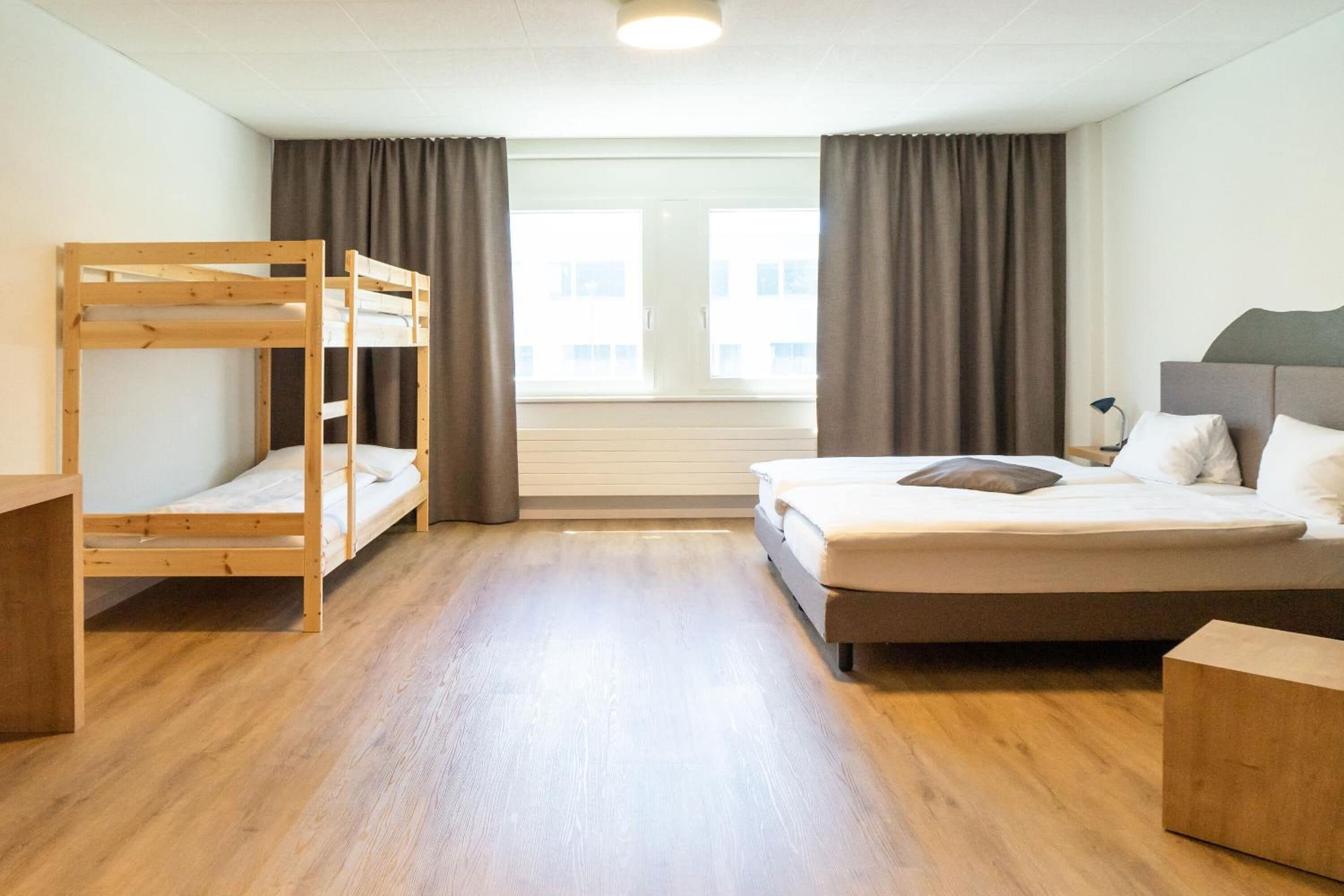 Ein Zimmer mit Etagenbett, einem Einzelbett, einem Schreibtisch und einem Fenster mit Vorhängen.