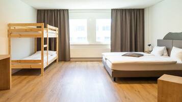 Ein Zimmer mit Etagenbett, einem Einzelbett, einem Schreibtisch und einem Fenster mit Vorhängen.
